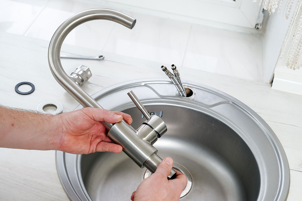 Person installing modern kitchen faucet over stainless steel sink.