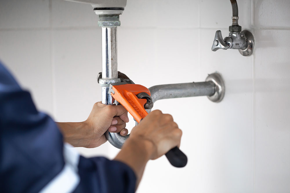 Plumber using wrench to repair sink pipe, close-up on hands and tools in a bathroom setting.