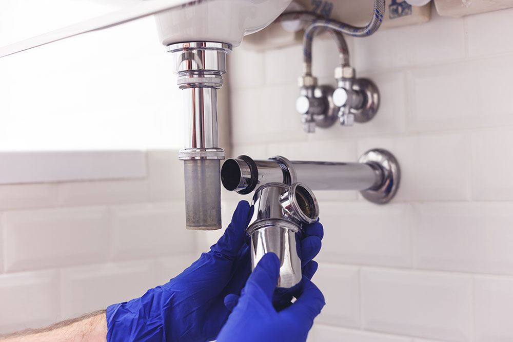 Plumber wearing blue gloves fixing a sink drain pipe in bathroom, close-up view.