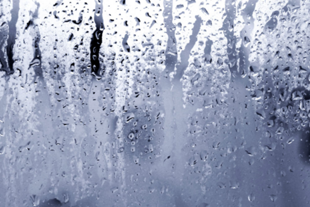Condensation on a foggy window creates water droplets and streaks, capturing a rainy, overcast atmosphere.