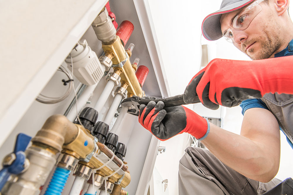 Plumber in red gloves fixing heating pipes with a wrench.