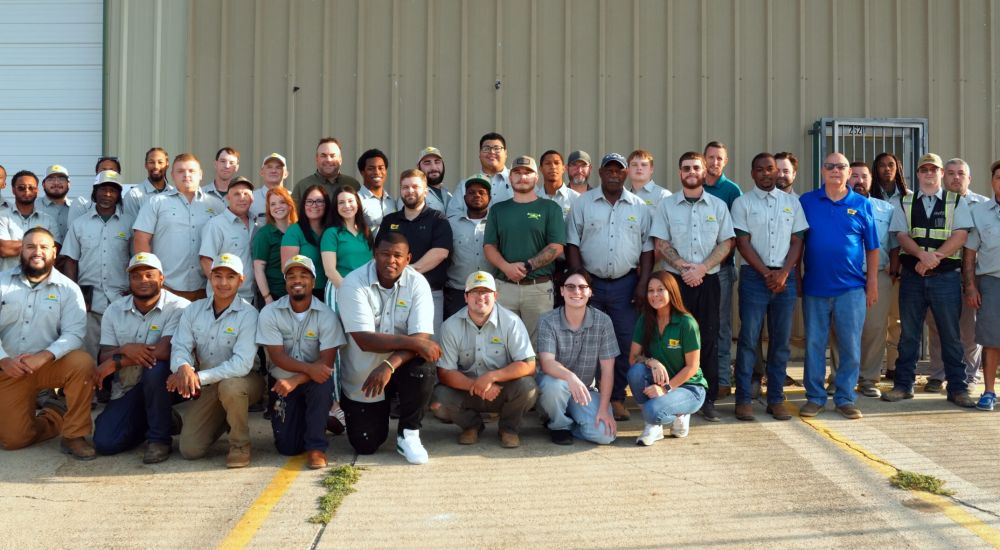 Group photo of diverse team members in uniform posing outdoors in front of a building.