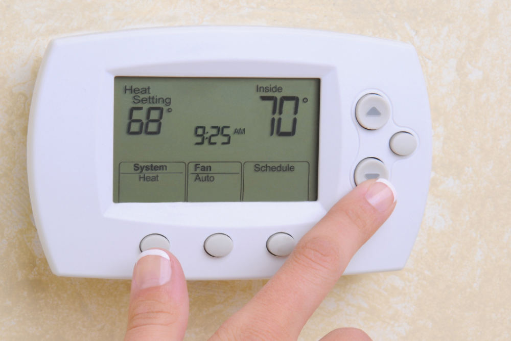 Finger adjusting wall-mounted digital thermostat showing 68°F heat setting and 70°F inside temperature.